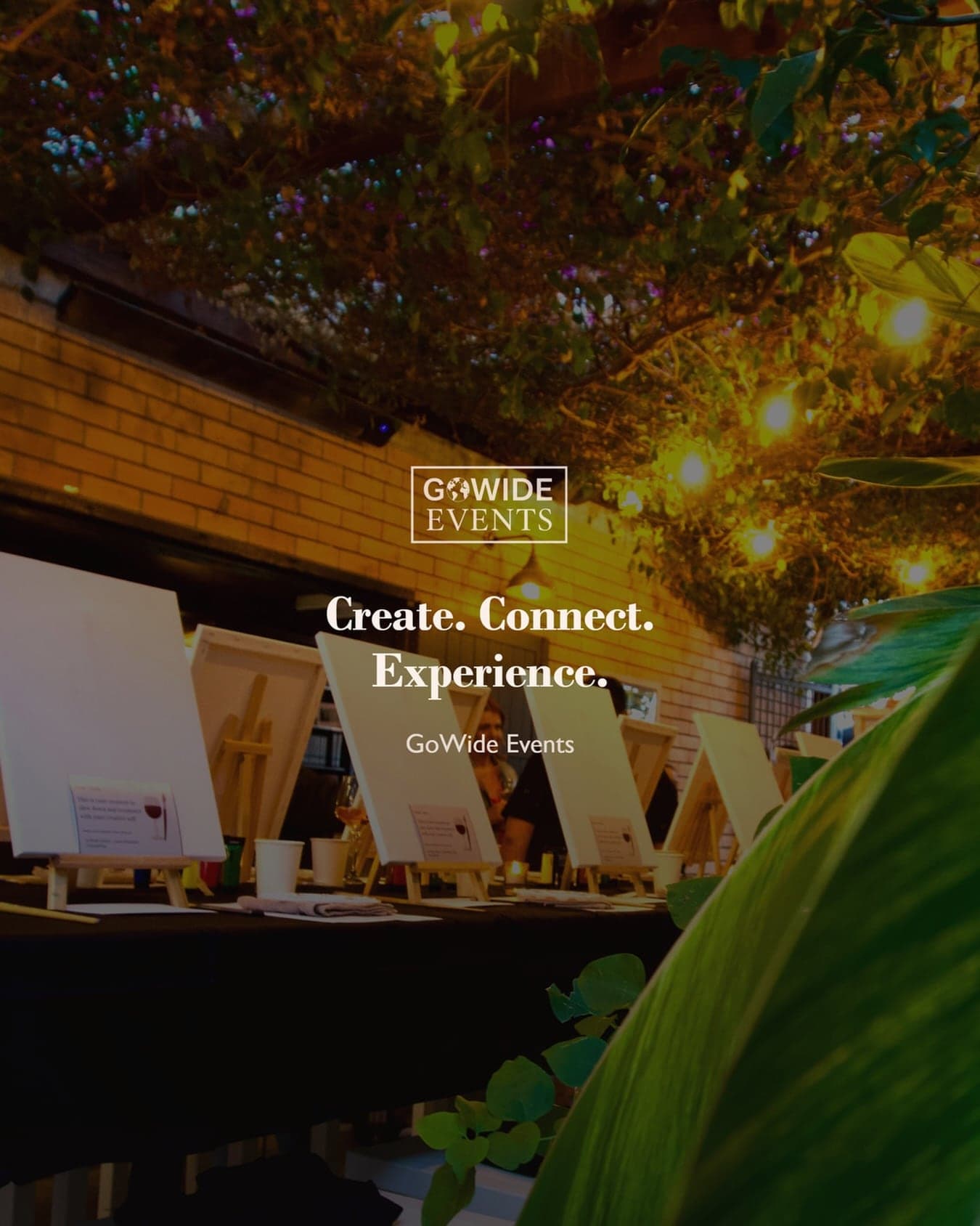 A table set with easels and canvases before guests arrive, under the words Create. Connect. Experience.