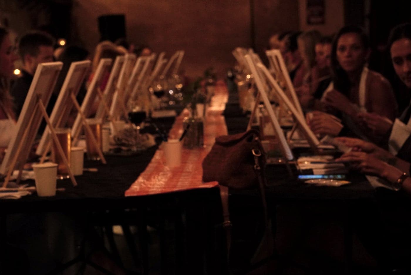 A long table full of painters at easels, candles along the runner.