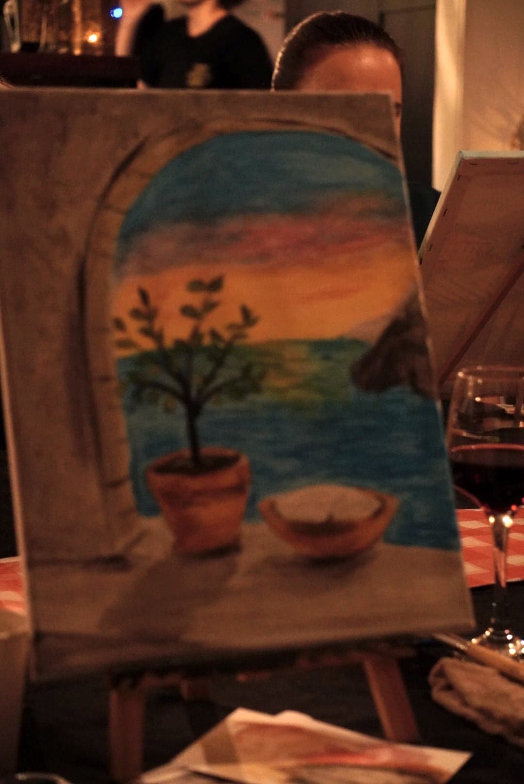A finished painting on an easel: a potted tree against a sunset sea.