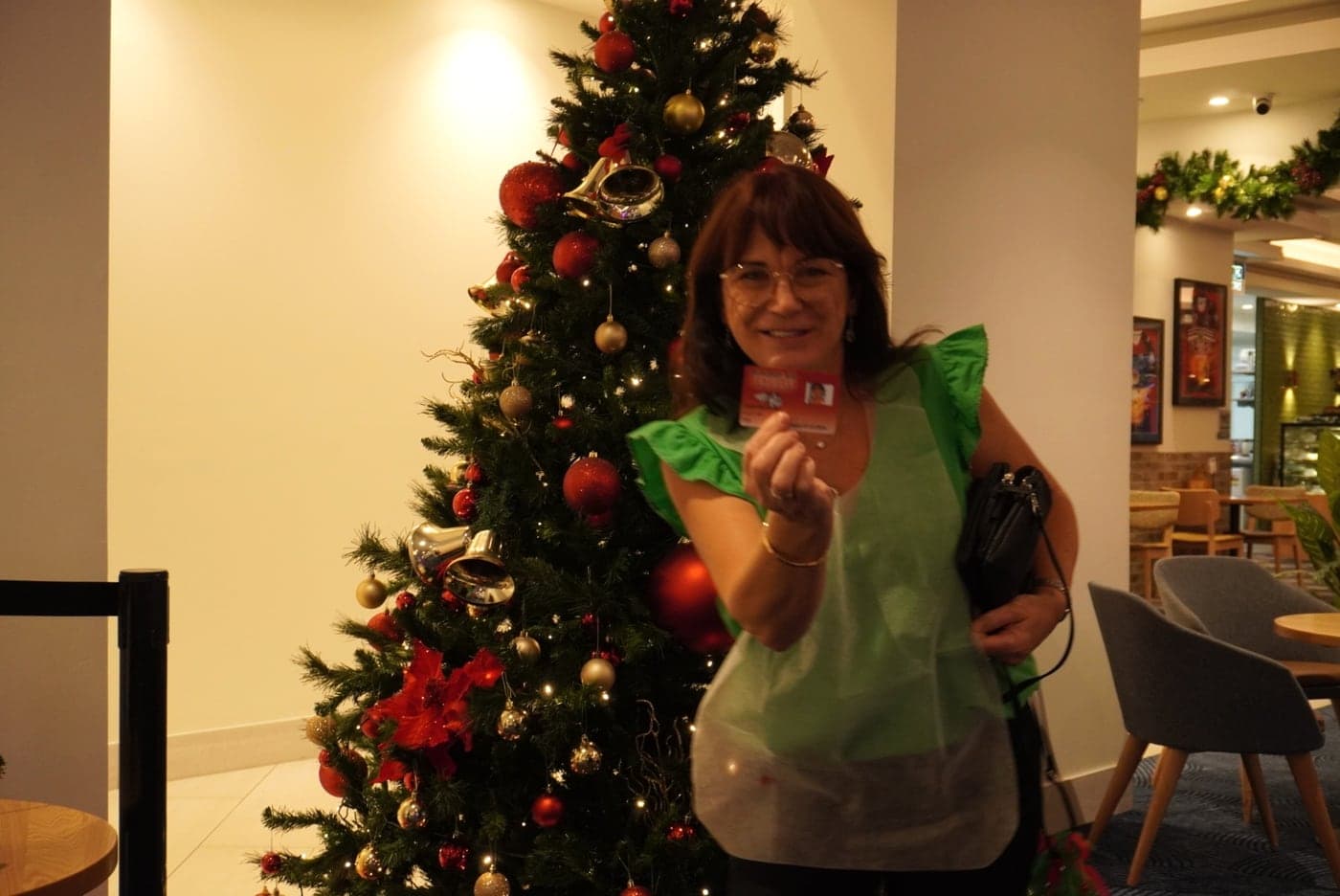 A guest in a painting apron smiling beside a decorated Christmas tree.