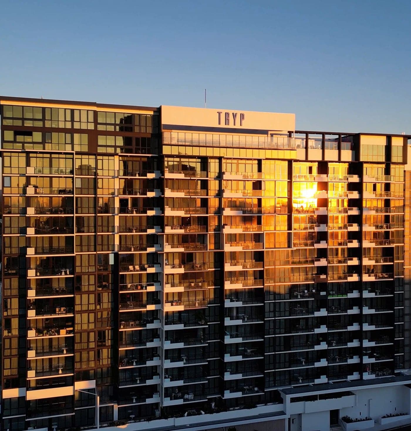 Toma con drone del TRYP by Wyndham Southport al atardecer, con la torre de vidrio encendida de dorado, en Gold Coast.