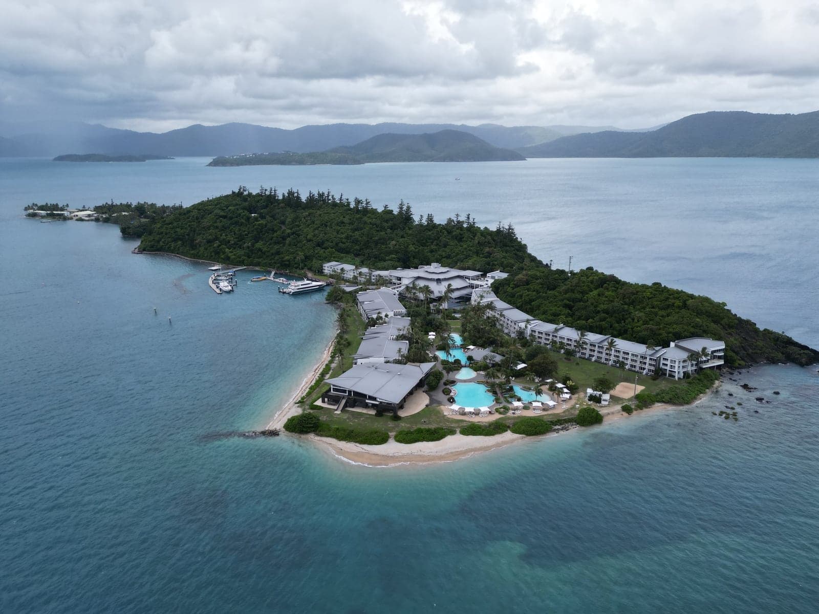Un resort isleño con piletas y muelle, rodeado de agua turquesa en las Whitsundays.