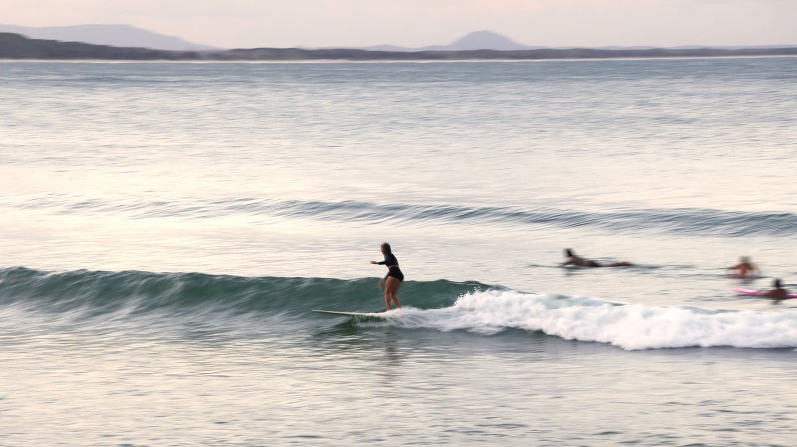 Una surfista en la punta de un longboard sobre una ola chica y de vidrio.