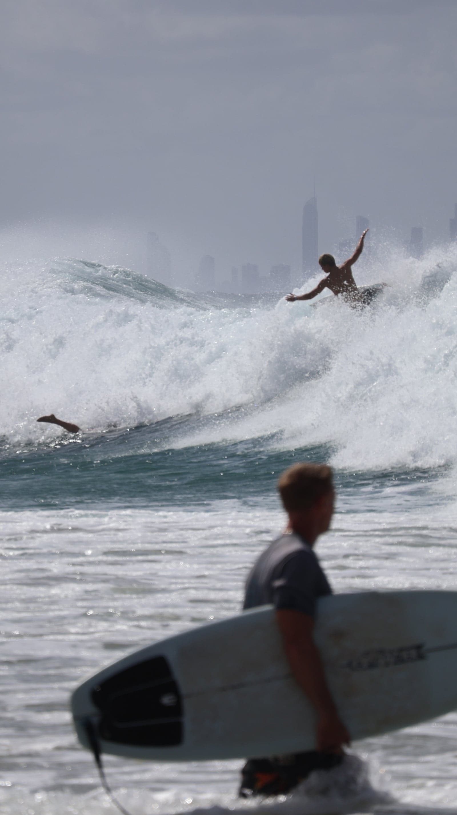 Un surfista en el aire saliendo de la ola, con el skyline de la Gold Coast detrás.