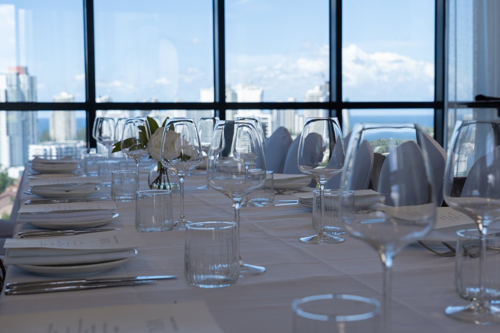 Una mesa larga preparada para el almuerzo de Skål en el TRYP Southport, con el skyline de Gold Coast detrás de los ventanales.