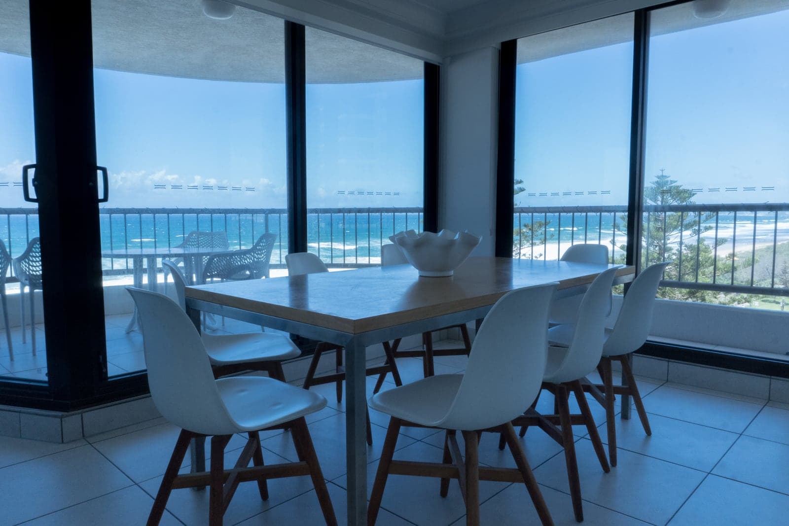 Una mesa para seis junto a ventanales de piso a techo, con el mar detrás del balcón — Boulevard North.