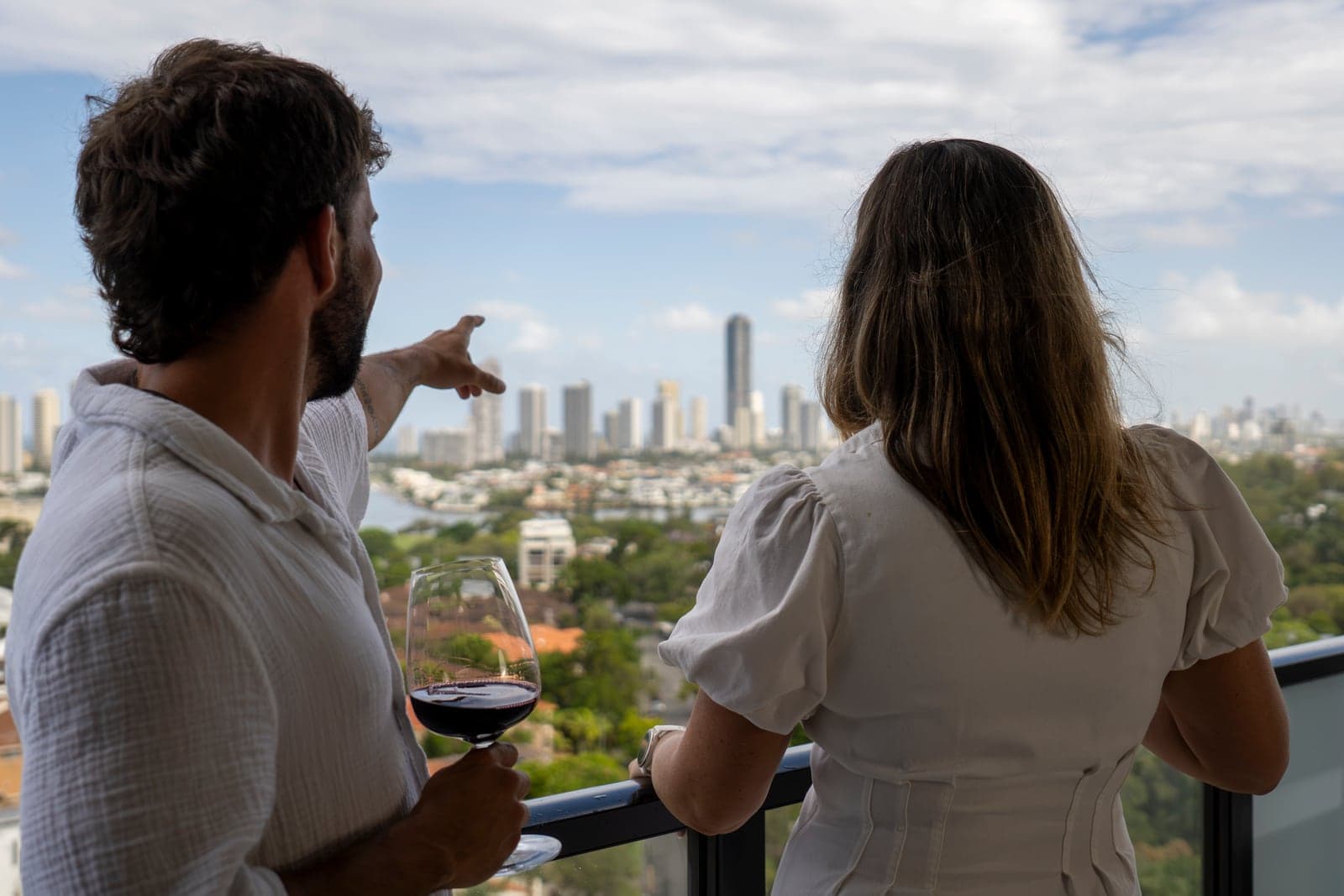 Una pareja con vino tinto en un balcón del TRYP Southport, señalando el skyline de Gold Coast.