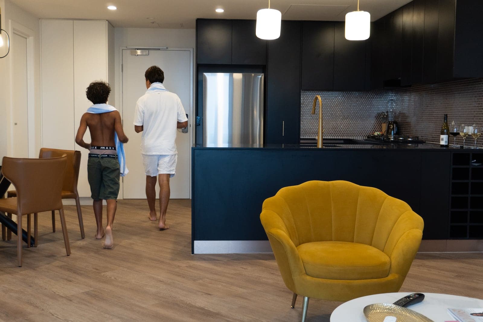 Dos chicos cruzando un departamento abierto del TRYP, entre la cocina y un sillón amarillo.